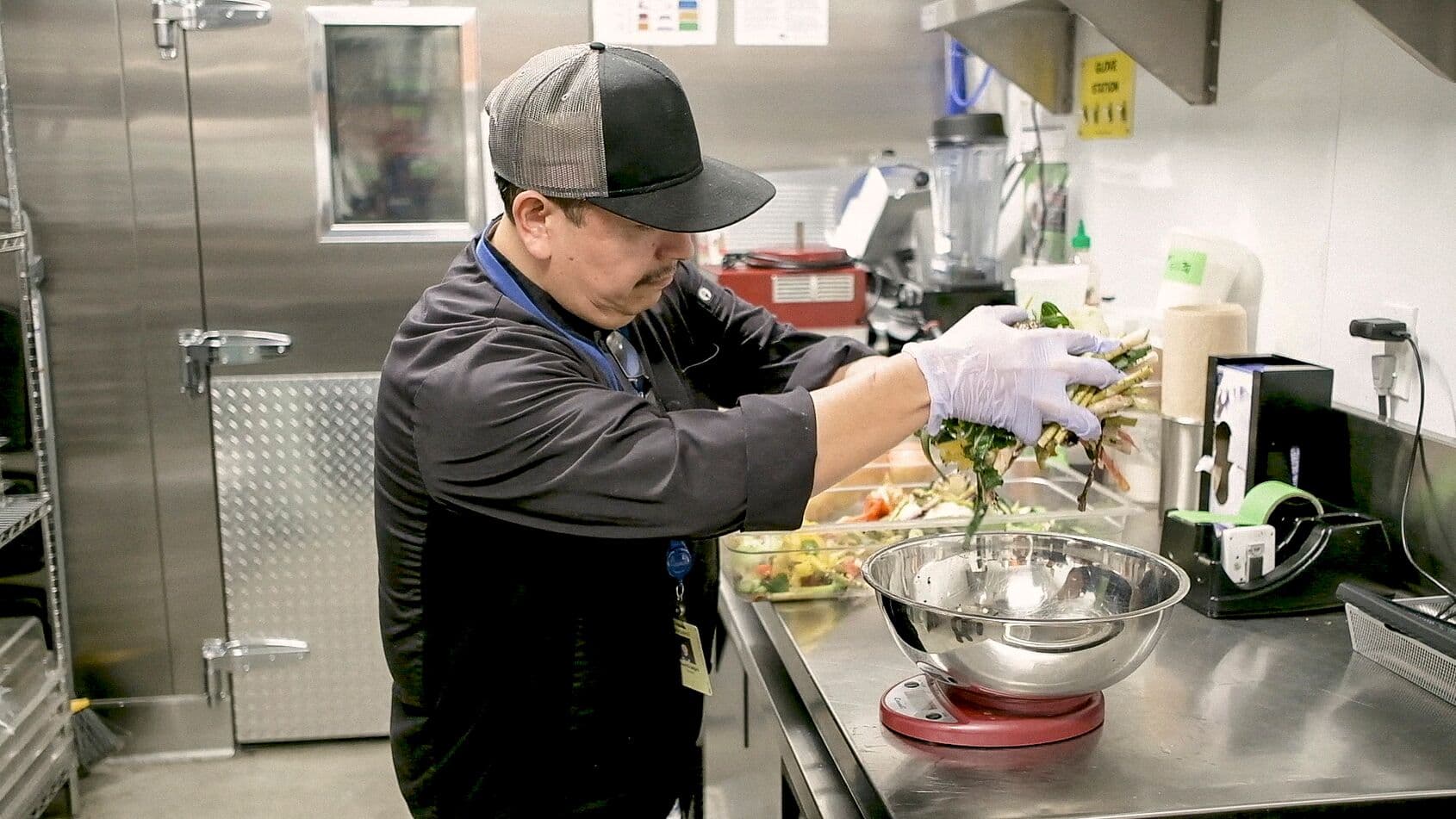 Chef weighs vegetable trimmings on a scale in a workplace dining kitchen to reduce food waste and  practice sustainability.